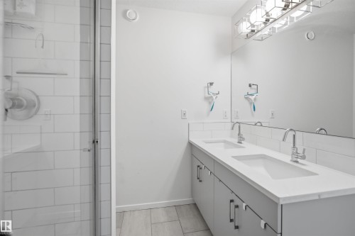 Bathroom featuring a double vanity with integrated sinks, a white countertop, and a large wall-mounted mirror - 7782 174A Avenue, Edmonton, AB - Indoor Photo Showing Bathroom