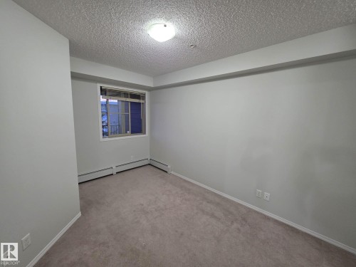 Carpeted room featuring a single window, white baseboards, and a textured ceiling - 206 12045 22 Avenue, Edmonton, AB - Indoor Photo Showing Other Room