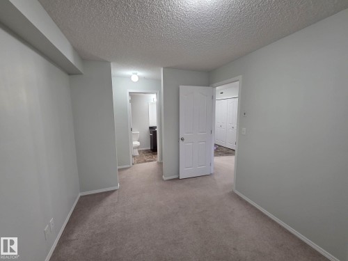 Carpeted interior space featuring light gray wall paint, white trim, and a textured ceiling - 206 12045 22 Avenue, Edmonton, AB - Indoor