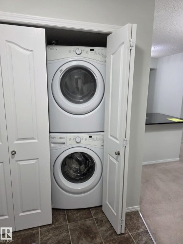 Dedicated laundry closet featuring a stacked white washer and dryer, bifold doors, and tile flooring - 206 12045 22 Avenue, Edmonton, AB - Indoor Photo Showing Laundry Room