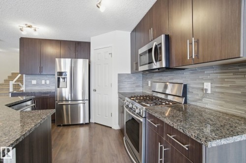 The kitchen features dark wood cabinetry, granite countertops, stainless steel appliances, and a tiled backsplash - 2553 Coughlan Road, Edmonton, AB - Indoor Photo Showing Kitchen With Upgraded Kitchen