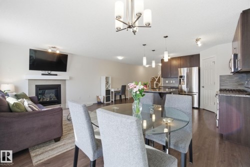Open concept living space featuring a living area with a fireplace, a dining area with a glass-top table, and a kitchen with stainless steel appliances and dark cabinetry - 2553 Coughlan Road, Edmonton, AB - Indoor With Fireplace