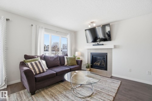 Living area featuring a fireplace with a light-colored tile surround, large windows, and dark wood-style flooring - 2553 Coughlan Road, Edmonton, AB - Indoor Photo Showing Living Room With Fireplace