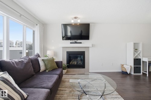 The living area features a fireplace with a light-colored tile surround, dark wood flooring, and large windows - 2553 Coughlan Road, Edmonton, AB - Indoor Photo Showing Living Room With Fireplace