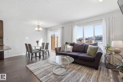 This open-concept living area features dark wood flooring, a dining space with a contemporary chandelier, and large windows providing ample natural light - 2553 Coughlan Road, Edmonton, AB - Indoor Photo Showing Living Room