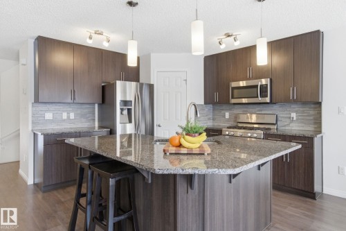 Kitchen featuring dark wood cabinetry, granite countertops, stainless steel appliances, and a central island with pendant lighting - 2553 Coughlan Road, Edmonton, AB - Indoor Photo Showing Kitchen With Upgraded Kitchen
