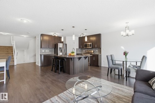 Expansive open concept living area featuring dark wood flooring throughout, a modern kitchen with stainless steel appliances, a center island with seating, and a dining area with a contemporary chandelier - 2553 Coughlan Road, Edmonton, AB - Indoor