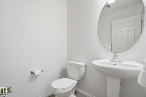 Bathroom featuring a white pedestal sink, a toilet, a round mirror, and light-colored walls - 2553 Coughlan Road, Edmonton, AB - Indoor Photo Showing Bathroom