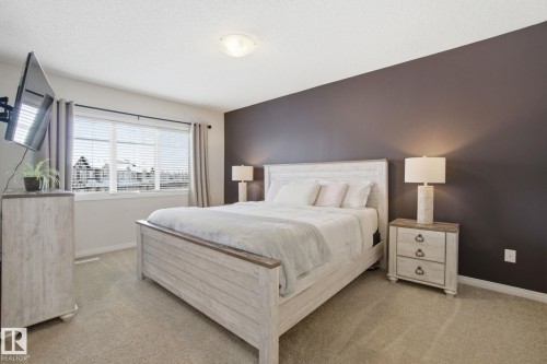 This room features light-colored carpeting, a broad window with blinds, and a neutral color palette with one accent wall - 2553 Coughlan Road, Edmonton, AB - Indoor Photo Showing Bedroom