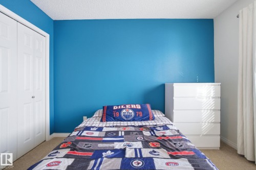 This room features a vibrant blue accent wall, a closet with bi-fold doors, and neutral carpeting - 2553 Coughlan Road, Edmonton, AB - Indoor Photo Showing Bedroom