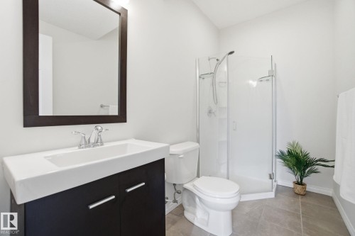 Bathroom featuring a dark wood vanity with a white countertop and rectangular sink, a framed mirror, a corner shower with a glass enclosure, and tiled floors - 2553 Coughlan Road, Edmonton, AB - Indoor Photo Showing Bathroom