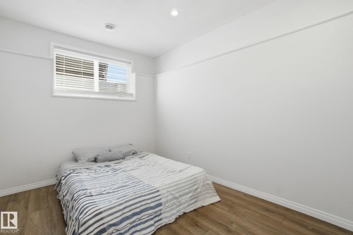 The room features bright white walls, a window with horizontal blinds, and warm-toned wood-style flooring - 2553 Coughlan Road, Edmonton, AB - Indoor Photo Showing Bedroom