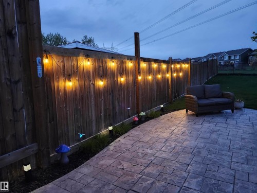 The property features a fenced yard with string lights, a paved patio area, and a lawn - 2553 Coughlan Road, Edmonton, AB - Outdoor