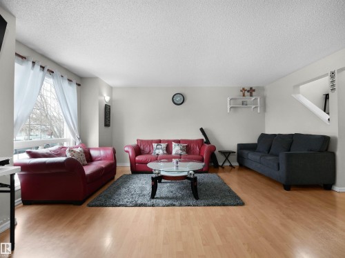 Bright open-concept living area featuring light wood-finish flooring, a large picture window with white sheer curtains, and light neutral wall colors - 21379 89 Avenue Nw, Edmonton, AB - Indoor Photo Showing Living Room