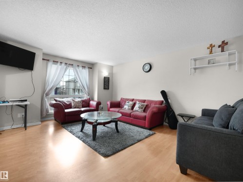 Bright living area featuring wood-finish flooring, a large window with sheer drapery, and a wall-mounted sconce - 21379 89 Avenue Nw, Edmonton, AB - Indoor Photo Showing Living Room