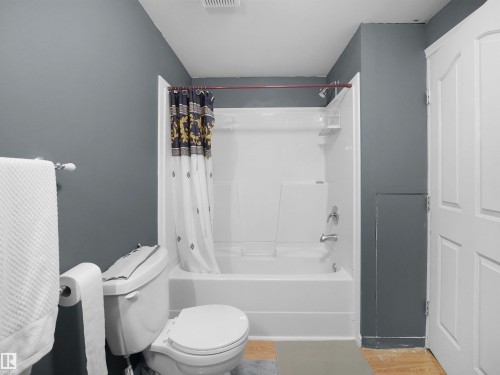 Bathroom featuring a white toilet, white bathtub with integrated shower, chrome fixtures, and a grey accent wall - 21379 89 Avenue Nw, Edmonton, AB - Indoor Photo Showing Bathroom