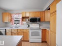 Kitchen featuring light wood cabinetry, a stainless steel over-the-range microwave, a white electric range, wood-finish flooring, and a double basin sink - 21379 89 Avenue Nw, Edmonton, AB  - Indoor Photo Showing Kitchen With Double Sink 