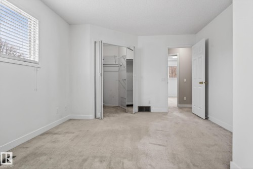 Carpeted room featuring a window with horizontal blinds, bi-fold closet doors, and a traditional hinged door - 18604 97A Avenue, Edmonton, AB - Indoor Photo Showing Other Room