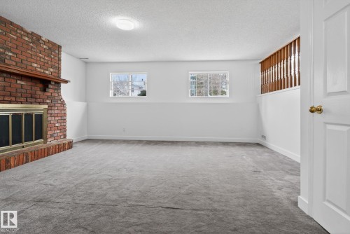 Spacious room featuring a brick fireplace with a wood mantle, two windows, carpet flooring, and white walls - 18604 97A Avenue, Edmonton, AB - Indoor With Fireplace
