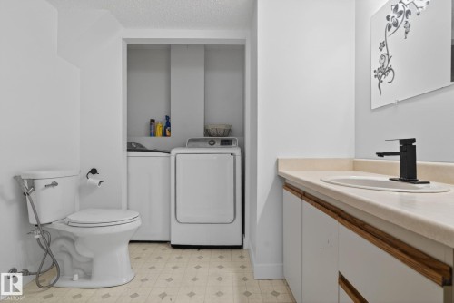 Bathroom featuring a white toilet, light-toned patterned flooring, and a vanity with white cabinetry, wood-finish handles, and a light-colored countertop with an undermount sink and a matte black faucet - 18604 97A Avenue, Edmonton, AB - Indoor Photo Showing Laundry Room
