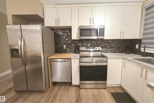 Kitchen featuring stainless steel appliances, white cabinetry, speckled countertops, and a mosaic tile backsplash - 4203 83 Street, Edmonton, AB - Indoor Photo Showing Kitchen