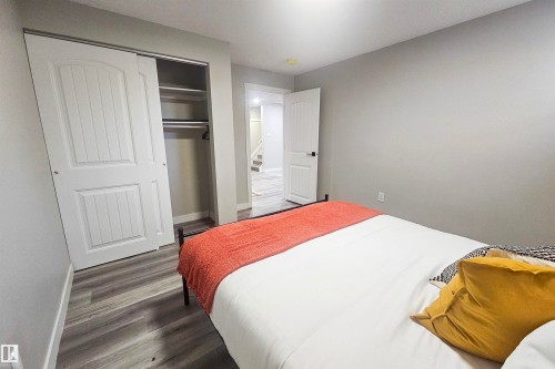 Spacious bedroom featuring wood-finish flooring, light grey wall paint, and a built-in closet with sliding panel doors - 4203 83 Street, Edmonton, AB - Indoor Photo Showing Bedroom