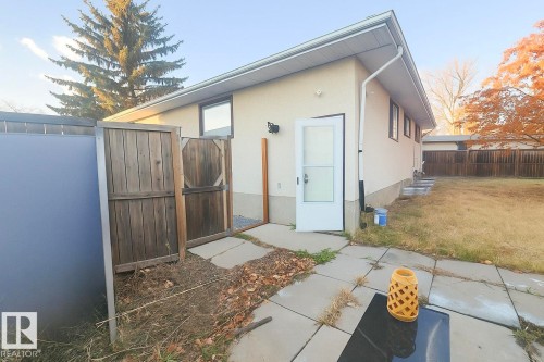 Rear exterior featuring stucco siding, multiple windows with dark trim, and a white storm door - 4203 83 Street, Edmonton, AB - Outdoor With Exterior