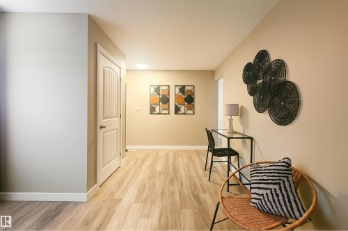 Hallway featuring wood-finish flooring, light-colored walls, white baseboards, and a white paneled door with brushed nickel hardware - 4203 83 Street, Edmonton, AB - Indoor Photo Showing Other Room