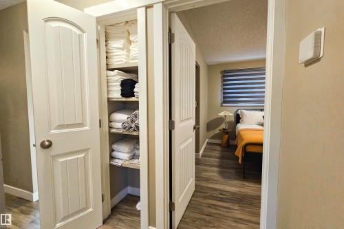 Hallway featuring a built-in linen closet with adjustable shelving, wood-finish flooring, and solid core doors with brushed nickel hardware - 4203 83 Street, Edmonton, AB - Indoor Photo Showing Other Room