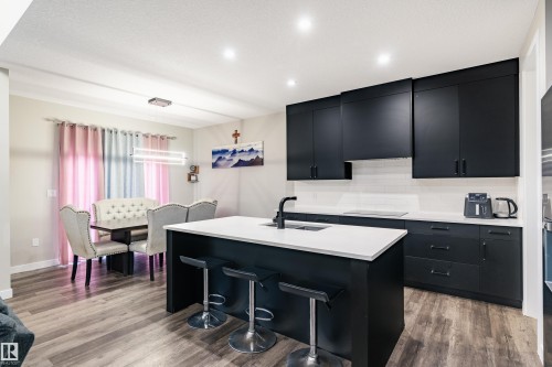 Modern kitchen featuring dark cabinetry, white countertops, a central island with integrated sink, and wood-finish flooring - 2 Edison Drive, St. Albert, AB - Indoor