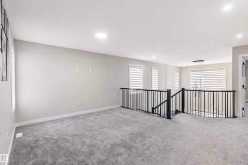 Spacious carpeted loft area with multiple windows, recessed lighting, and a contemporary black metal railing - 2 Edison Drive, St. Albert, AB - Indoor Photo Showing Other Room