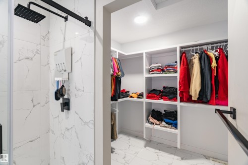 Walk-in closet with integrated shelving and hanging rods, accompanied by a shower featuring white marble-look tiling, a matte black rainfall shower head, and a matte black shower control - 2 Edison Drive, St. Albert, AB - Indoor With Storage
