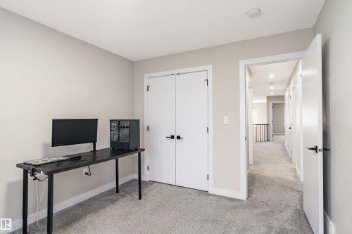 Carpeted room with light neutral wall paint, featuring a white bi-fold closet door with black hardware and a white interior door leading to a hallway with recessed lighting - 2 Edison Drive, St. Albert, AB - Indoor Photo Showing Other Room