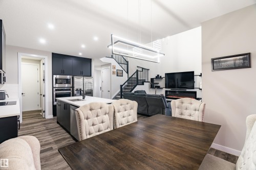 Open-concept living space featuring a modern kitchen with a large island, stainless steel appliances, wood-finish flooring, and a contemporary linear chandelier - 2 Edison Drive, St. Albert, AB - Indoor