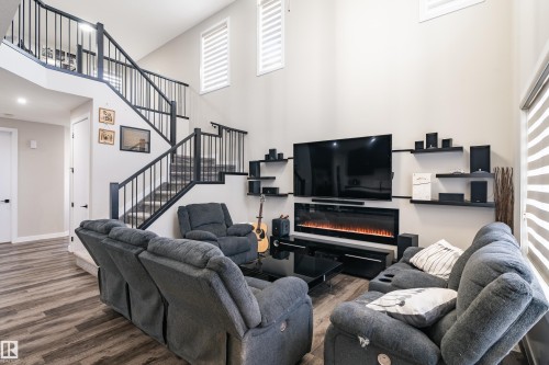 Spacious living area featuring high ceilings, wood-finish flooring, a contemporary linear fireplace, and a striking black spindle staircase with a matching upper-level railing - 2 Edison Drive, St. Albert, AB - Indoor