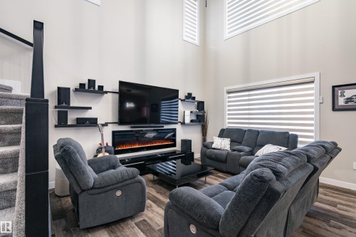 Living space featuring soaring ceilings, a linear electric fireplace, wood-finish flooring, and built-in wall shelving - 2 Edison Drive, St. Albert, AB - Indoor Photo Showing Other Room With Fireplace