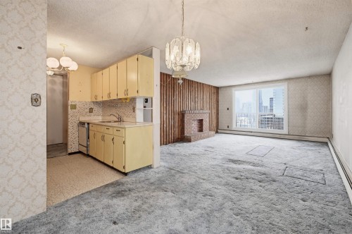 Spacious interior featuring a large window, a brick-clad fireplace, and an adjacent kitchen area with light-toned cabinetry and a tiled backsplash - 701 10135 116 Street Nw, Edmonton, AB - Indoor