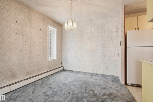 Dining area featuring a decorative chandelier, baseboard heating, a single window, and an adjacent kitchen with built-in cabinetry and a refrigerator - 701 10135 116 Street Nw, Edmonton, AB - Indoor