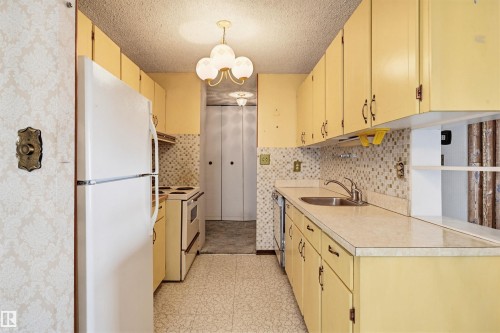 Galley kitchen featuring yellow cabinetry, laminate countertops, mosaic tile backsplash, and a built-in sink - 701 10135 116 Street Nw, Edmonton, AB - Indoor Photo Showing Kitchen