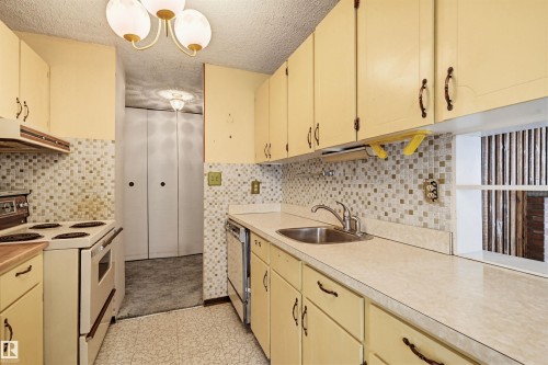 Kitchen featuring extensive cabinetry, patterned tile backsplash, integrated sink with faucet, white appliances, and patterned floor tile - 701 10135 116 Street Nw, Edmonton, AB - Indoor Photo Showing Kitchen