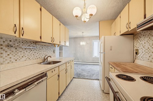 Galley kitchen featuring light-toned cabinetry, mosaic tile backsplash, a stainless steel sink, and durable laminate countertops - 701 10135 116 Street Nw, Edmonton, AB - Indoor Photo Showing Kitchen
