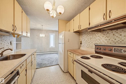 Galley kitchen featuring light-colored cabinetry, white appliances, and a mosaic tile backsplash - 701 10135 116 Street Nw, Edmonton, AB - Indoor Photo Showing Kitchen