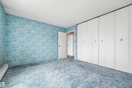 Room featuring blue patterned wallpaper, full wall of bi-fold white closet doors, white interior door, and blue carpet flooring - 701 10135 116 Street Nw, Edmonton, AB - Indoor Photo Showing Other Room