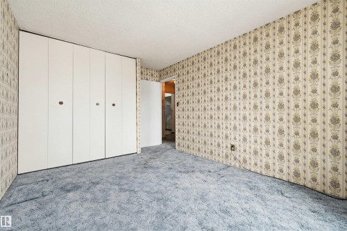 Spacious interior with full-wall bi-fold closet doors, patterned wallpaper, textured ceiling, and soft blue carpeting - 701 10135 116 Street Nw, Edmonton, AB - Indoor Photo Showing Other Room