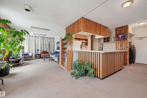Interior space featuring wood paneling accents, light beige carpeting, and a built-in bar with slatted wood detailing - 701 10135 116 Street Nw, Edmonton, AB - 