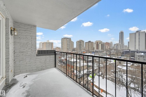Private balcony with a metal railing, featuring a stucco-textured wall and an outdoor light fixture - 701 10135 116 Street Nw, Edmonton, AB - Outdoor