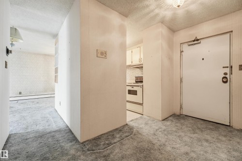 Entryway featuring a white door with security hardware, textured wall finishes, ceiling-mounted light fixture, and carpet flooring - 701 10135 116 Street Nw, Edmonton, AB - Indoor Photo Showing Other Room