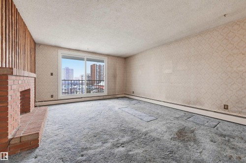 Living area featuring a brick fireplace with a wood-slat accent wall, textured wallpaper, and a large sliding glass door with a balcony - 701 10135 116 Street Nw, Edmonton, AB - Indoor Photo Showing Other Room With Fireplace