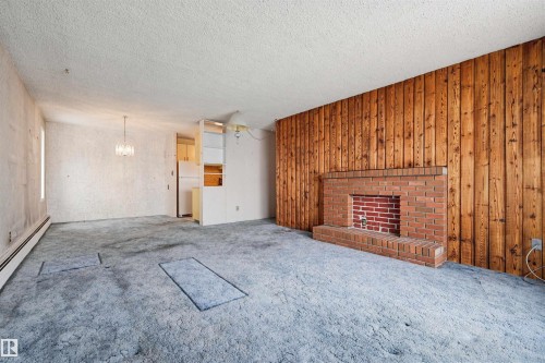 Room featuring a red brick fireplace with a wood-paneled accent wall, textured ceiling, and wall-to-wall carpeting - 701 10135 116 Street Nw, Edmonton, AB - Indoor Photo Showing Other Room