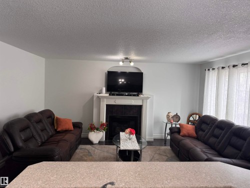 The living area features a fireplace with a white mantel and dark tile surround, dark flooring, and light-colored walls - 1115 61 Street, Edmonton, AB - Indoor Photo Showing Living Room With Fireplace
